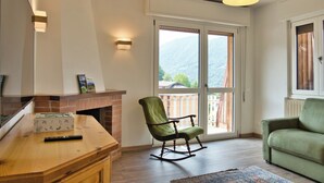 Une pièce avec une cheminée, un fauteuil à bascule, un canapé et une grande fenêtre donnant sur les montagnes.