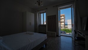 Una camera da letto con un letto, un armadio, una scrivania e un balcone che si affaccia su degli edifici.