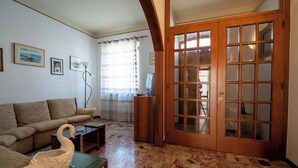 Un soggiorno con un divano, un tavolino in vetro, una scultura a forma di cigno, una televisione e una porta in legno con vetri.