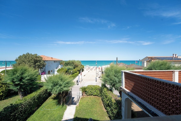 A coastal hotel with a view of the sea, a paved walkway, and greenery.