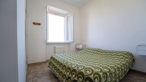 Un dormitorio con cama, ventana, radiador y un interruptor de luz instalado en la pared.