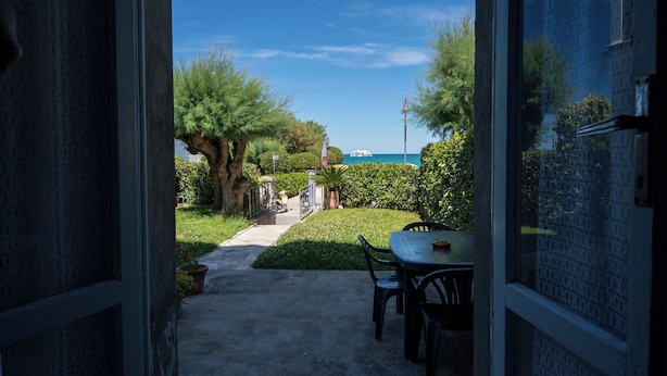 Un umbral abierto que da a un patio con una mesa y sillas, un sendero y vista al mar.