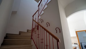 Una escalera con barandilla de madera y balaustradas de metal rojas, que lleva a un área de cocina con estufa y lavadora.