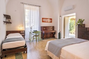 Ein Schlafzimmer mit zwei Betten, einem Klavier, einem Schreibtisch mit Stuhl und einem Fenster mit Vorhängen.