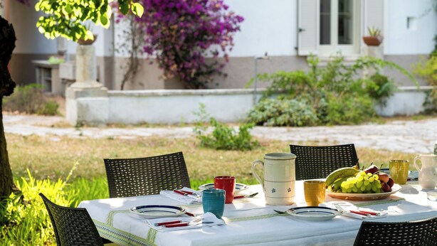 An outdoor dining table with chairs, a pitcher, a bowl of fruit, and a white building in the background. - Dimora Lustrelle con parco privato (Cutrofiano)