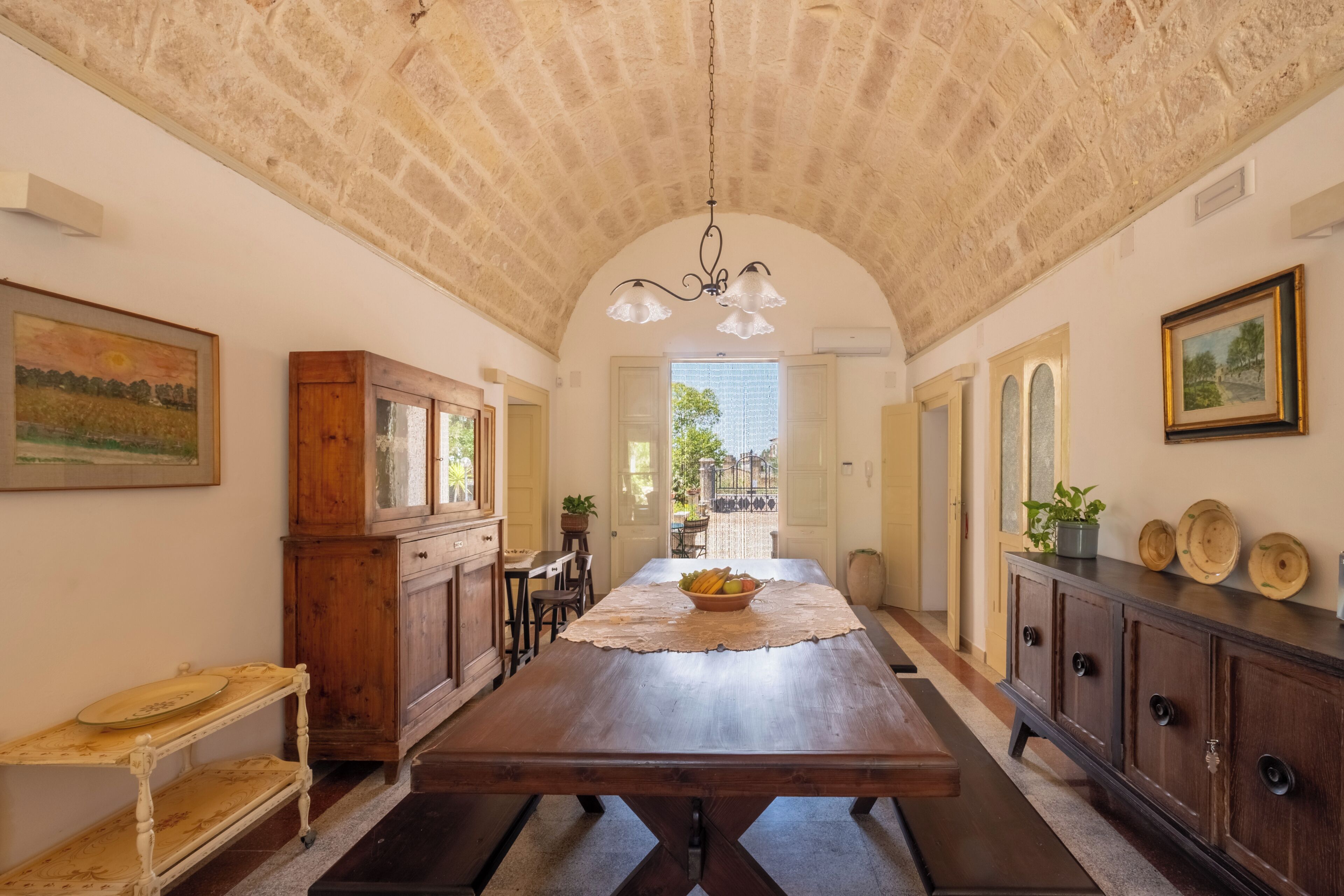 A spacious dining area with a long wooden table, a chandelier, and rustic stone ceiling.