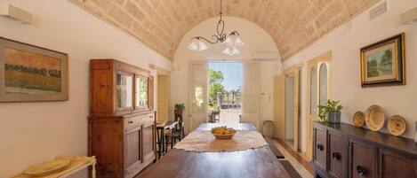 A spacious dining area with a long wooden table, a chandelier, and rustic stone ceiling.