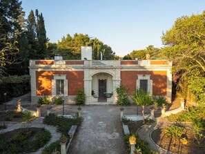 A building with a symmetrical facade, a central entrance, and a surrounding garden with potted plants and a gravel path. - Dimora Lustrelle con parco privato (Cutrofiano)