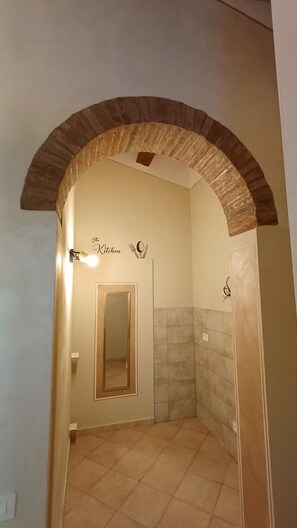 Een badkamer met betegelde vloer, een spiegel, een handdoekhouder en een bordje met de tekst 'The Kitchen'.