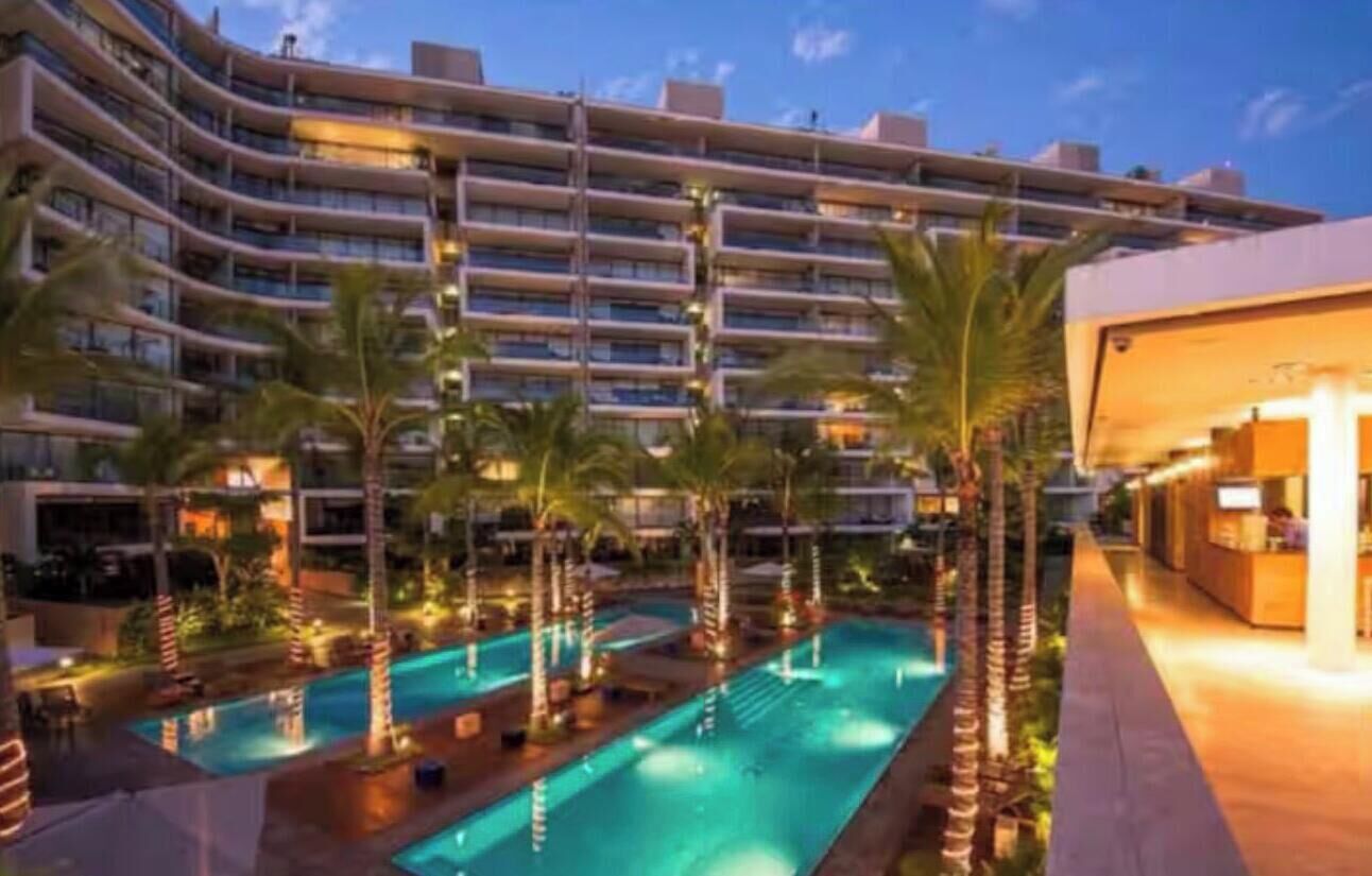 Un hôtel à plusieurs étages doté d’une piscine entourée de palmiers.