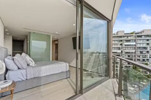 A modern bedroom with a bed, a fan, and a view of a cityscape through large glass windows. - Brand-New Nima Bay High-Rise Apartment by the Beautiful Marina (Puerto Vallarta)