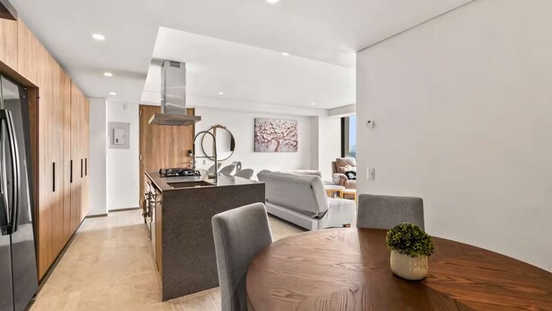 Una cocina moderna con una isla central, una mesa de comedor con sillas y un sofá gris al fondo.