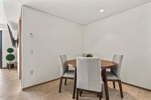 Uma sala de jantar com uma mesa redonda, quatro cadeiras cinza estofadas e um pequeno vaso com planta.