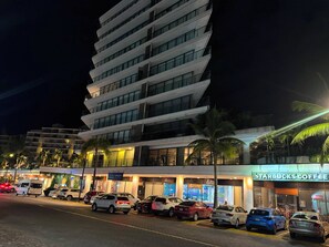 A multi-story hotel with a modern design, featuring a row of parked cars and a Starbucks Coffee shop in front. - Brand-New Nima Bay High-Rise Apartment by the Beautiful Marina (Puerto Vallarta)