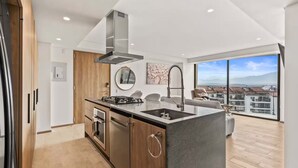 Une cuisine moderne dotée d’un îlot central, d’appareils électroménagers en acier inoxydable et d’une grande fenêtre offrant une vue sur la ville.