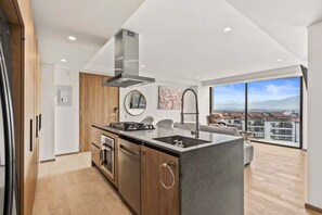 Eine moderne Küche mit einer zentralen Kochinsel, Edelstahlgeräten und einem großen Fenster mit Blick auf die Stadt.