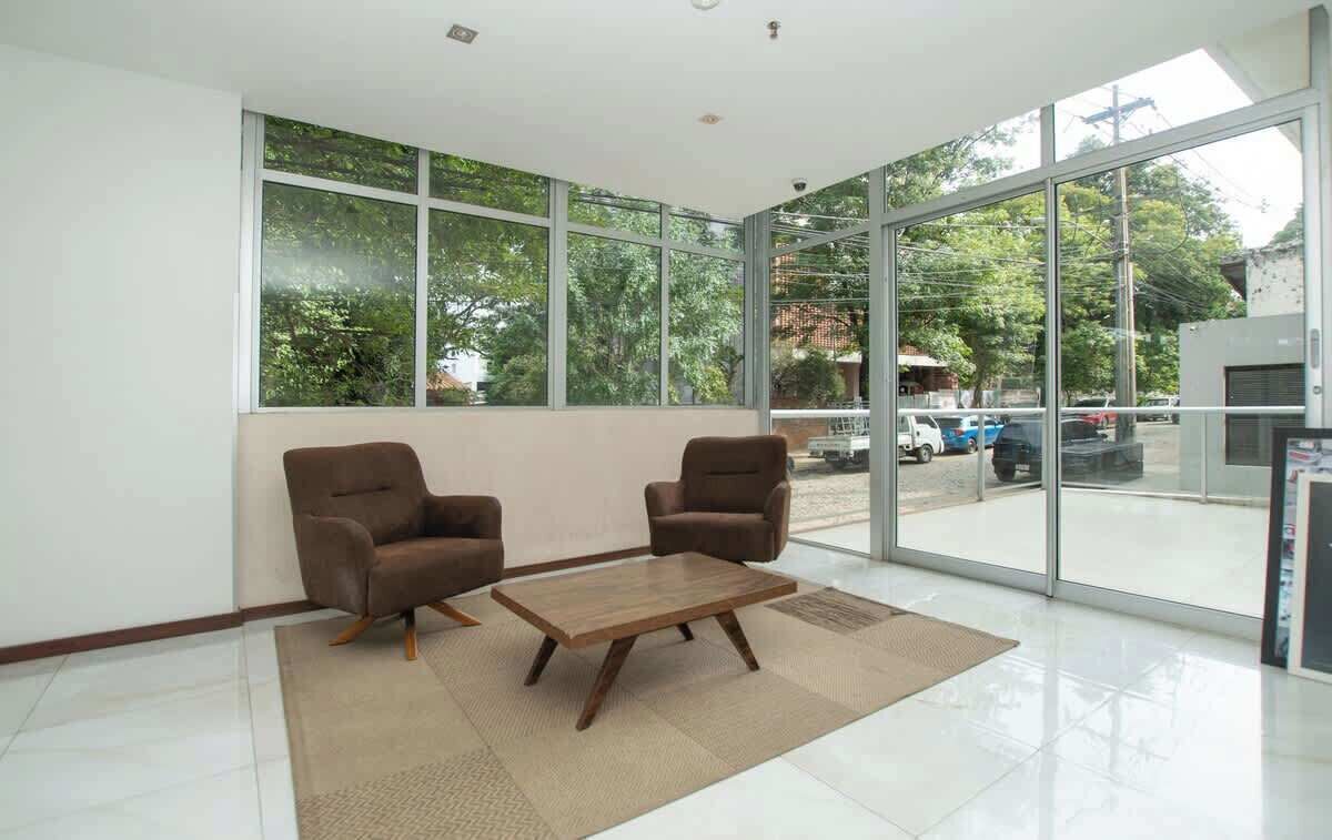 A spacious room with large windows, two brown armchairs, a wooden coffee table, and a tiled floor.