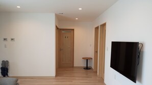 A hallway with wooden flooring, a grey sofa, a small round table, and a mounted TV. - Fuyu no Sonata 2 (Nakafurano)