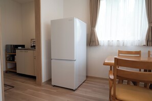 Een kleine keuken met een witte koelkast, houten keukenkastjes en een eettafel met stoelen.