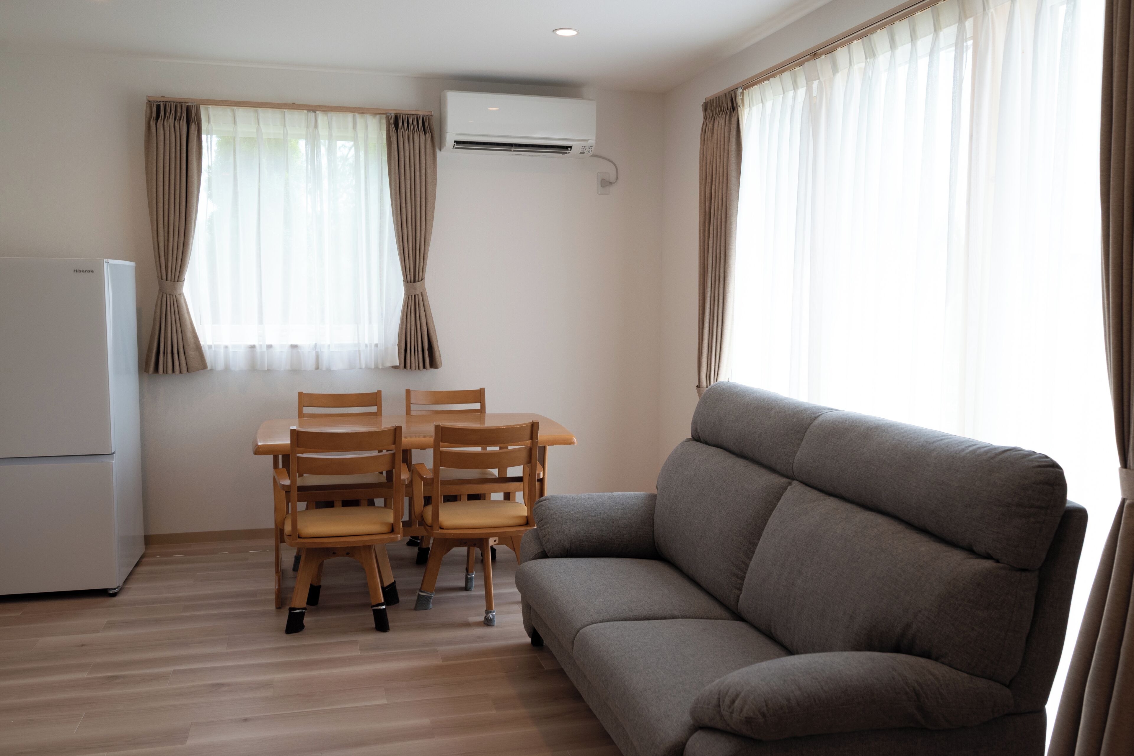 A living room with a sofa, a dining table with chairs, an air conditioning unit, and a refrigerator.