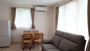 A living room with a sofa, a dining table with chairs, an air conditioning unit, and a refrigerator. - Fuyu no Sonata 2 (Nakafurano)