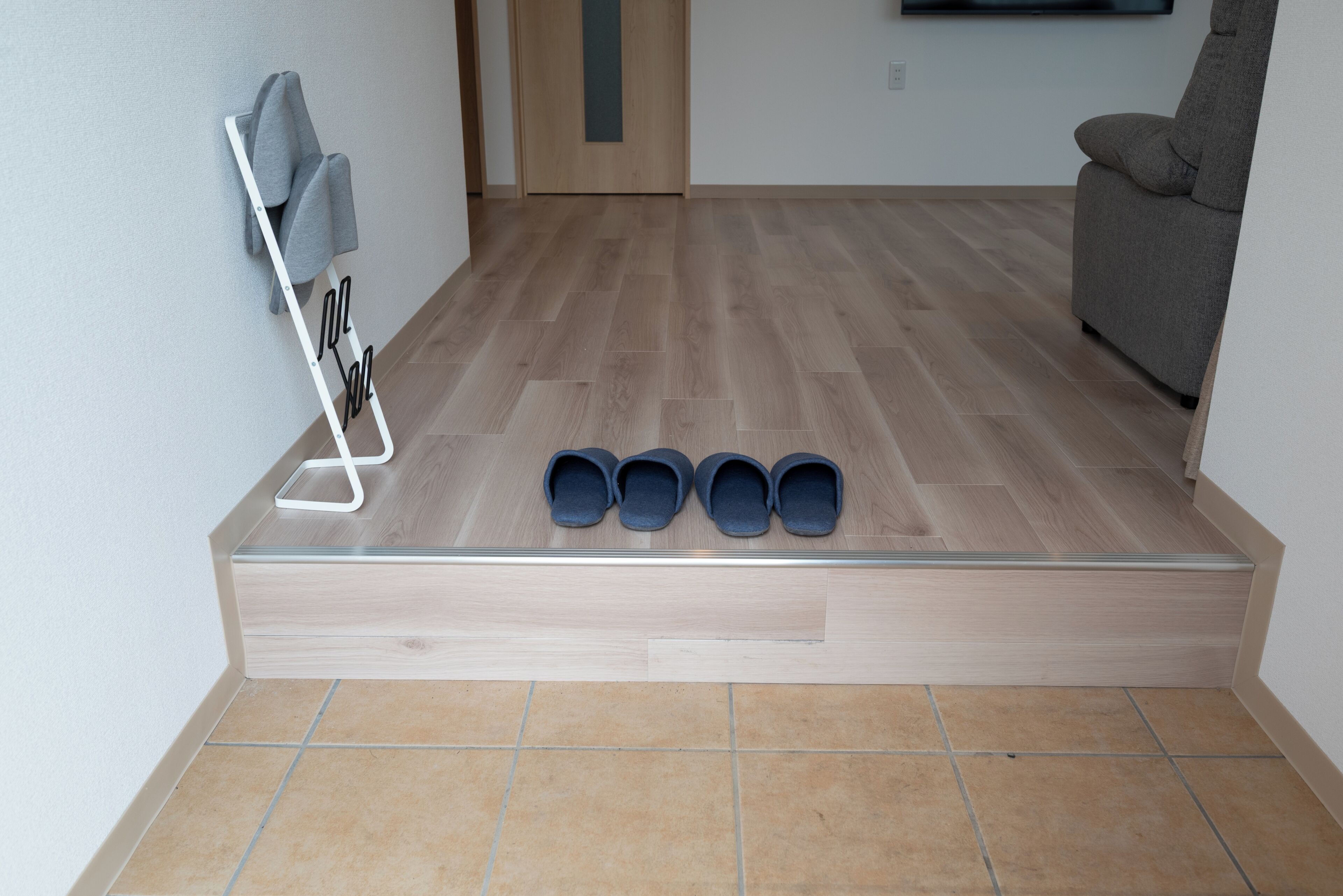Una habitación con piso de madera, un sofá gris y un zapatero con cuatro pares de zapatos.