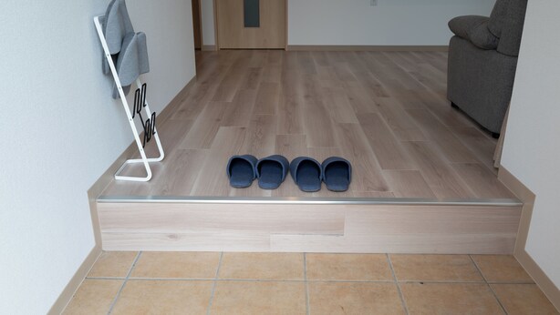 A room with a wooden floor, a grey sofa, and a shoe rack with four pairs of shoes. - Fuyu no Sonata 2 (Nakafurano)