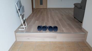 Una habitación con piso de madera, un sofá gris y un zapatero con cuatro pares de zapatos.