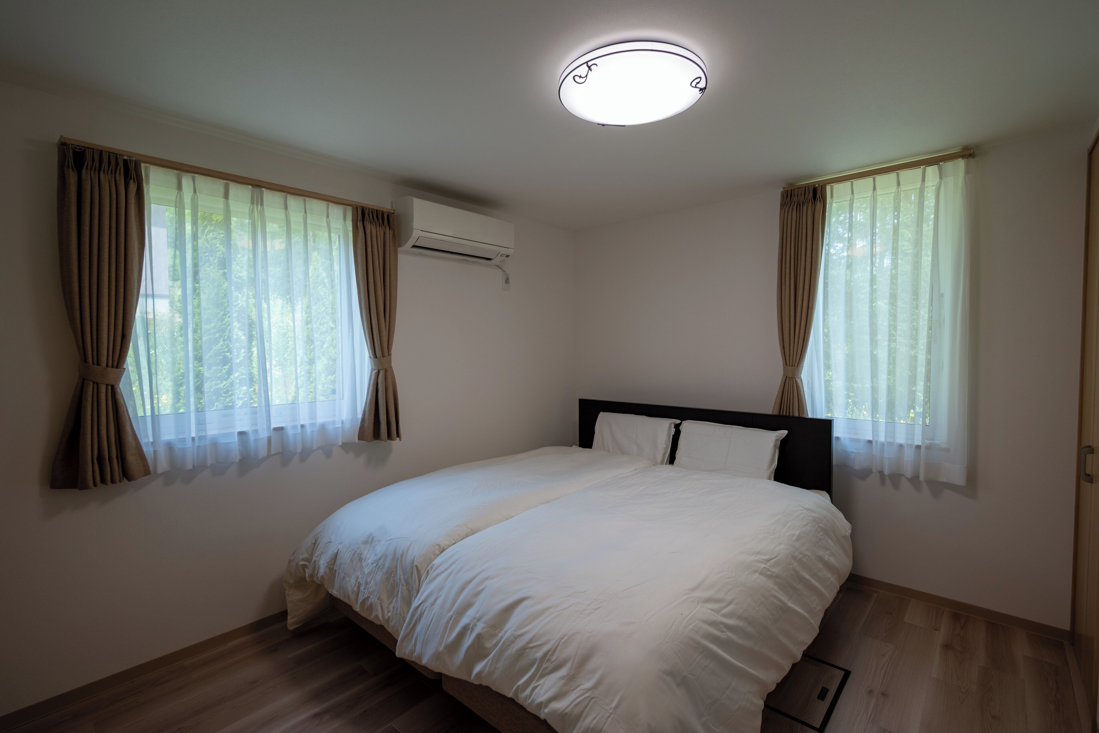 Un dormitori amb un llit, cortines, un aparell d'aire condicionat i una làmpada al sostre.
