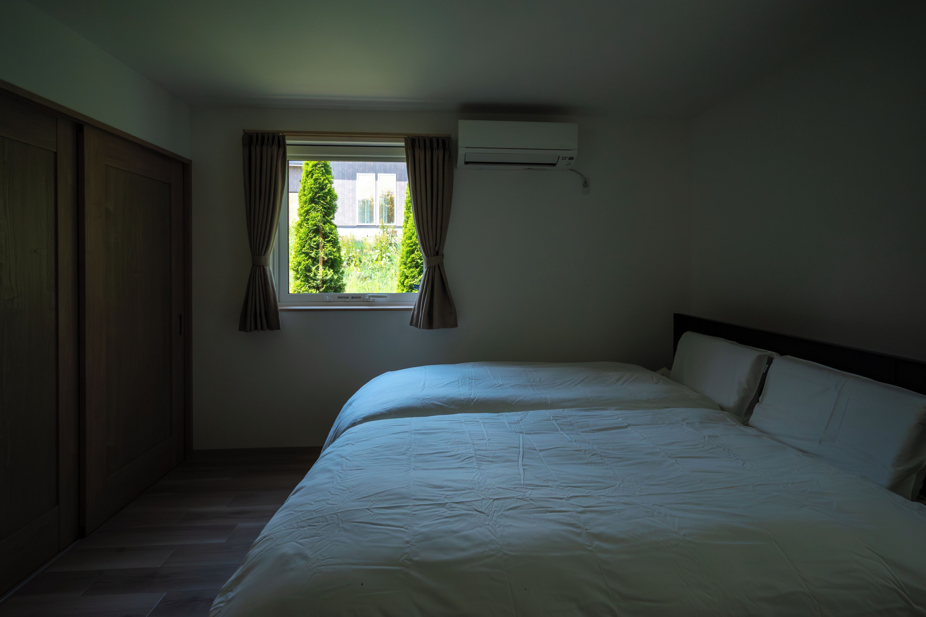 Een slaapkamer met een groot bed, een raam met gordijnen, een airconditioning en een houten garderobe.