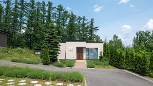 A modern building with a wooden door, surrounded by a forested area. - Fuyu no Sonata 2 (Nakafurano)