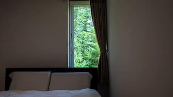 A bedroom with a bed, a window with curtains, and a view of greenery outside.