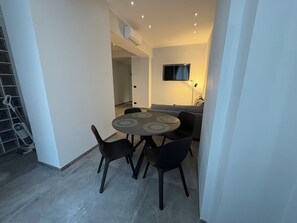 A dining area with a round table, four chairs, a flat-screen TV mounted on the wall, and a staircase in the background. - Bilocale nel cuore di Genova (Genova)
