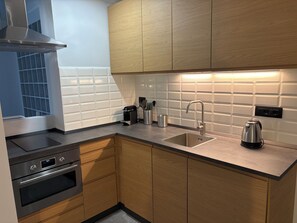 A modern kitchen with wooden cabinets, a stainless steel sink, a kettle, and a built-in oven. - Bilocale nel cuore di Genova (Genova)