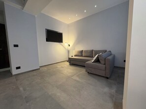 A modern living room with a sofa, a flat-screen TV, and recessed ceiling lighting. - Bilocale nel cuore di Genova (Genova)