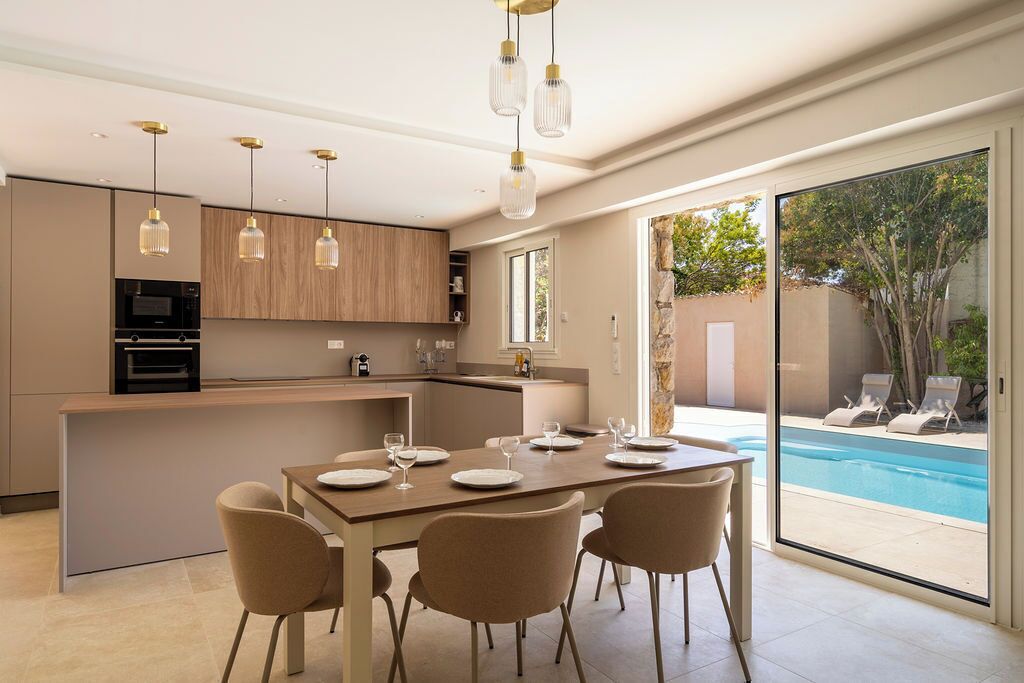 Une cuisine moderne dotée d’appareils électroménagers intégrés, un coin repas avec une table dressée pour quatre personnes, et une vue sur une piscine.