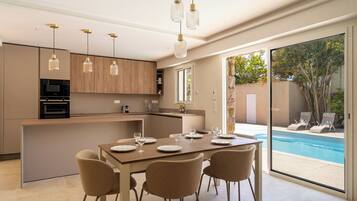 Une cuisine moderne dotée d’appareils électroménagers intégrés, un coin repas avec une table dressée pour quatre personnes, et une vue sur une piscine.
