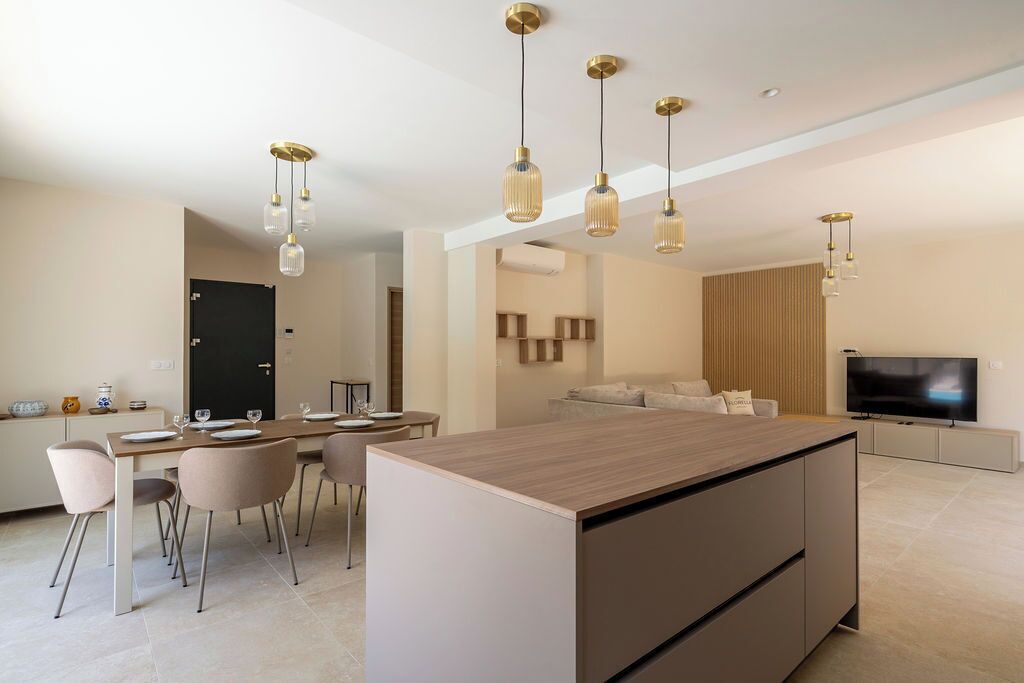 A modern kitchen with a central island, dining area with chairs, and a TV in the living room.