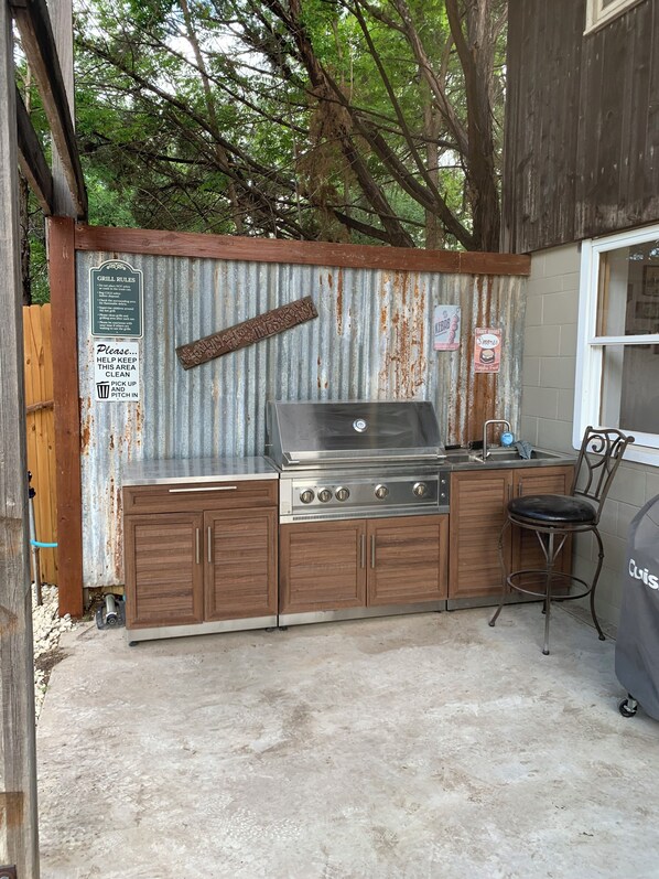 An outdoor kitchen with a grill, wooden cabinets, and a metal chair.