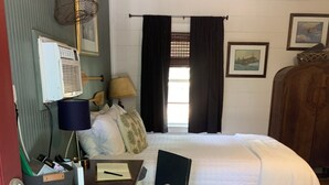 Ein Schlafzimmer mit Bett, Schreibtisch, Stuhl, Lampe, Kleiderschrank und einem Fenster mit Vorhängen.