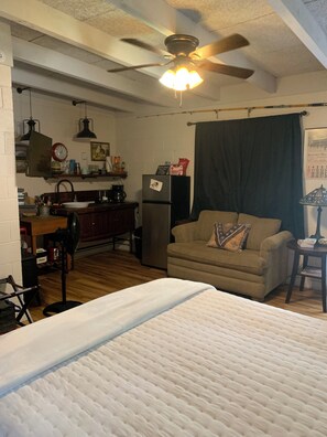 A compact living space with a kitchenette, a bed, a ceiling fan, and a couch.
