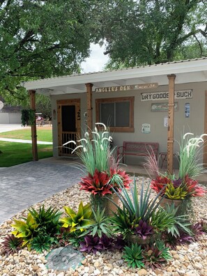 A building with a wooden porch, a sign reading 'Angler's Den Minnows 58', and a variety of colorful plants in front.