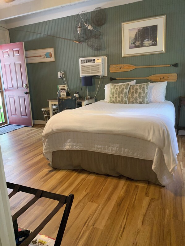 A bedroom with a large bed, a desk, a chair, a wall-mounted air conditioner, and a door.