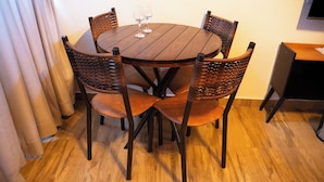 Una mesa redonda de madera con cuatro sillas de mimbre, dos copas de vino y una mesita a la derecha.