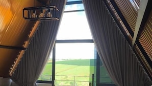 Una habitación con techo inclinado, un sofá, una mesita y vistas a un paisaje verde a través de grandes ventanales.