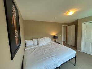 Een slaapkamer met een bed, nachtkastje, een ingelijste foto en een deur die naar een andere kamer leidt.