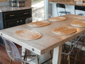 Una mesa de comedor de madera con individuales tejidos y sillas transparentes.