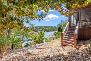 Una escalera de madera que conduce a una zona cubierta con vistas a un lago, árboles y cielo despejado.