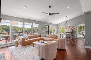 Amplia sala de estar con un sofá grande, una mesa de centro y una mesa de comedor con sillas. Cuenta con un ventilador de techo y vistas a una terraza con mobiliario exterior.