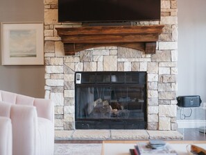 A stone fireplace with a wooden mantel, a framed picture on the wall, and a sofa in the foreground.